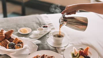 A breakfast setting with croissants, waffles, and fruit on plates, a cup of coffee being poured, and a table with a vase of flowers.