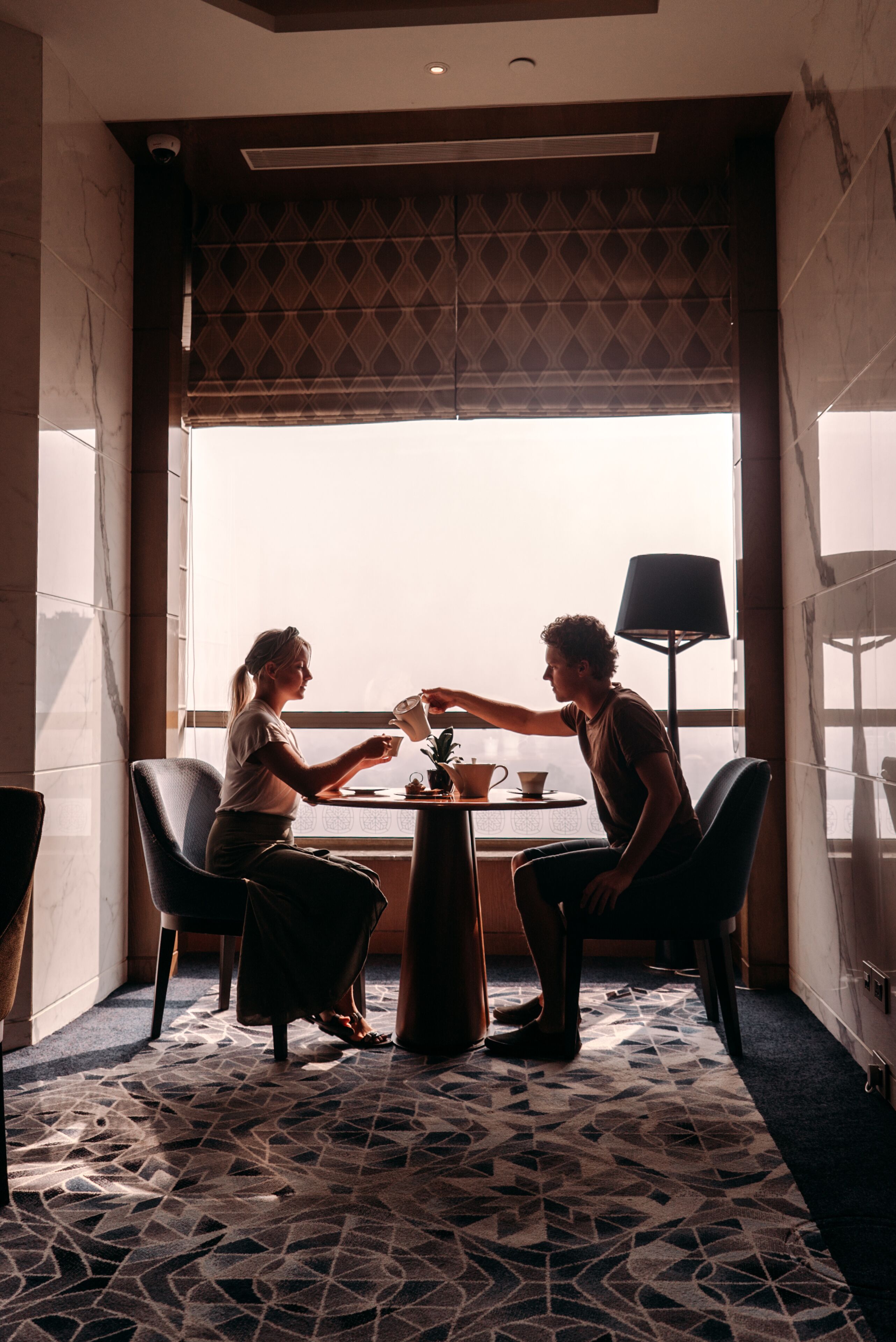 A hotel room with a large window, a patterned floor, and a table with two chairs.