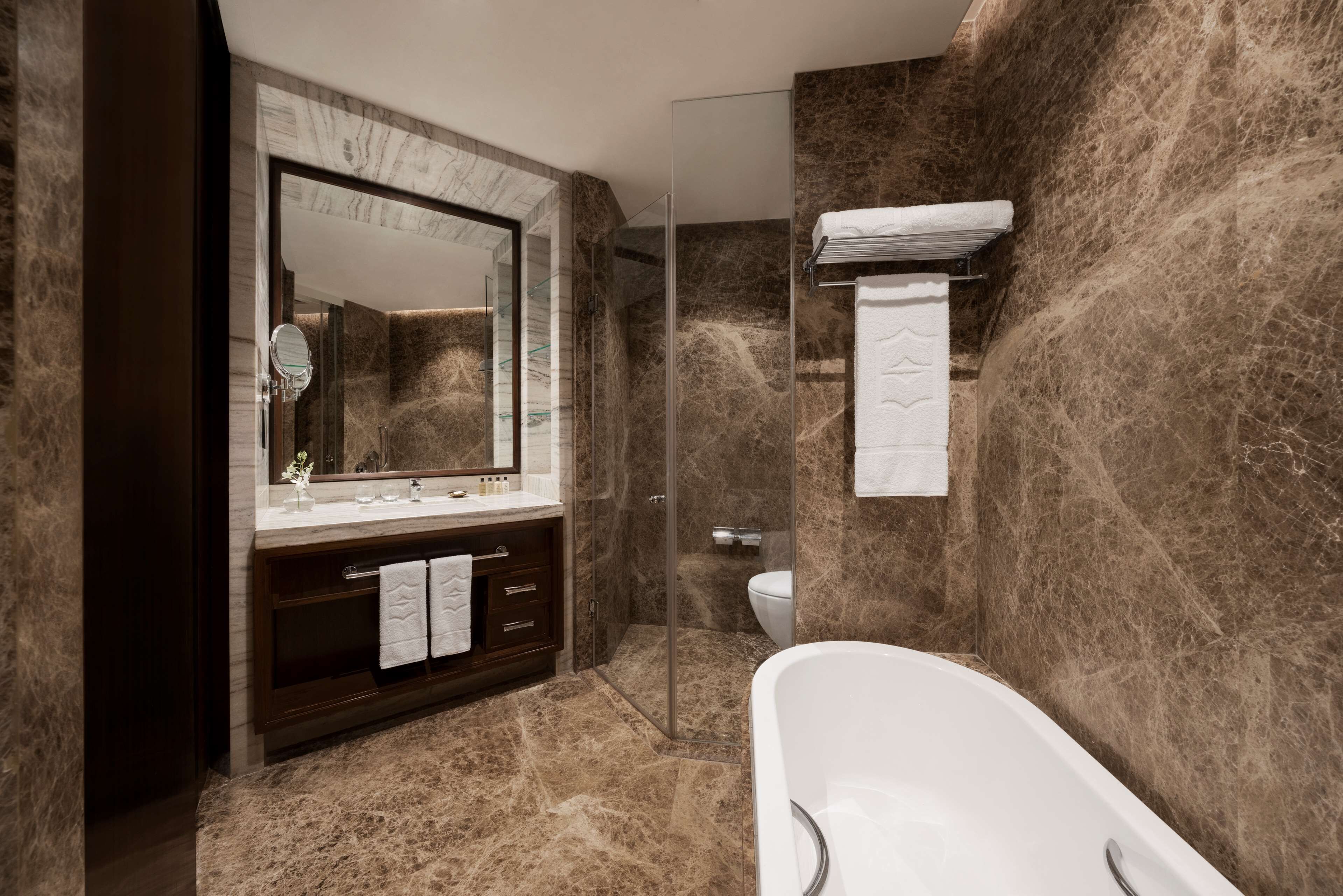 A modern bathroom with a marble floor, a freestanding bathtub, a large mirror, and a glass-enclosed shower.