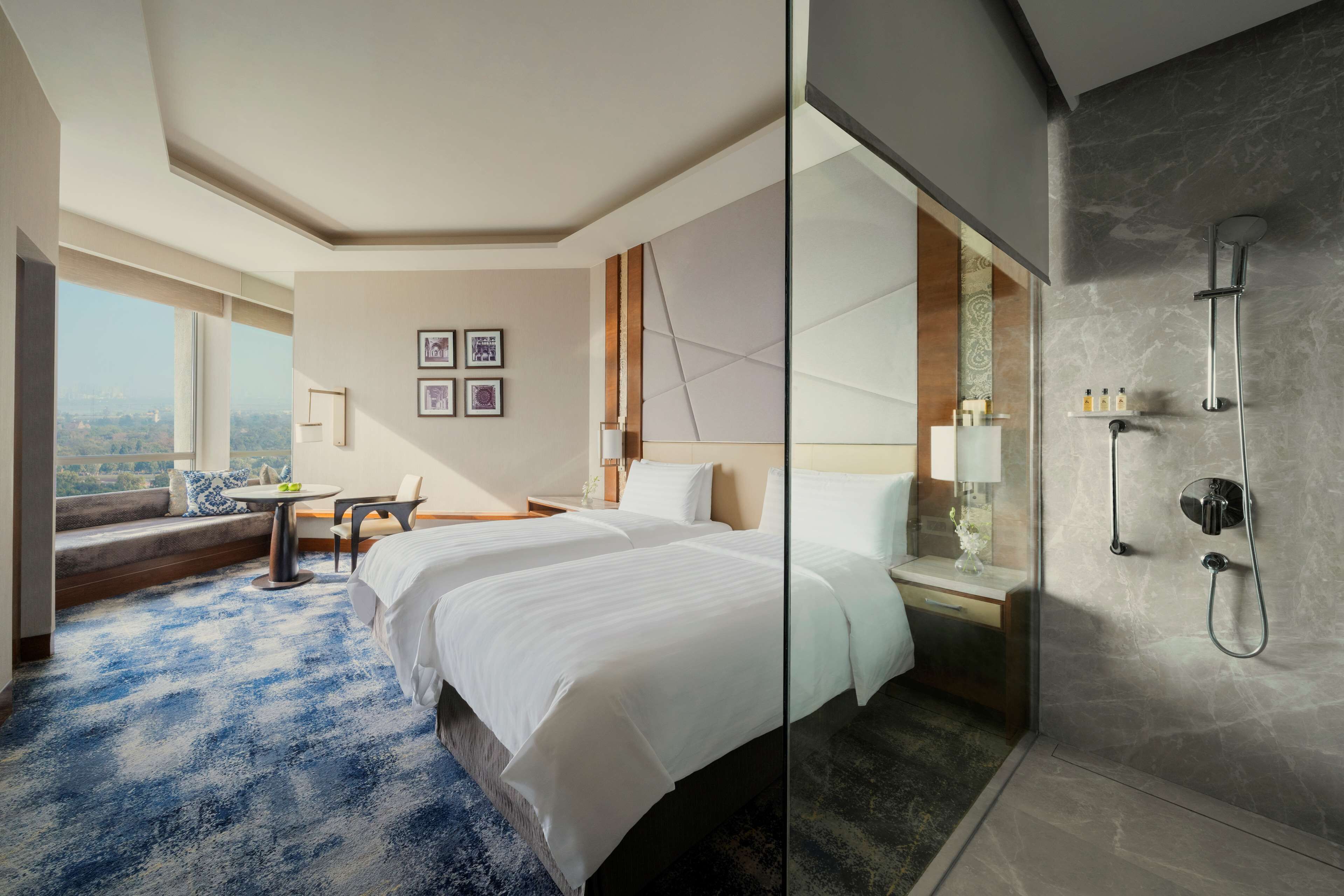 Hotelkamer met een groot bed, een zithoek met uitzicht, een douchegedeelte met glazen wand en stadszicht door het raam.