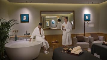 A spa room with a large bathtub, a massage table, and a mirror.