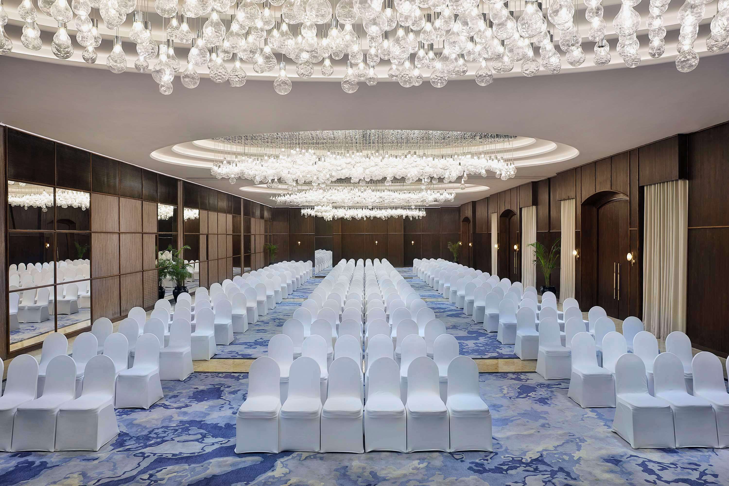 A conference room with rows of white chairs, a blue patterned carpet, and a chandelier.