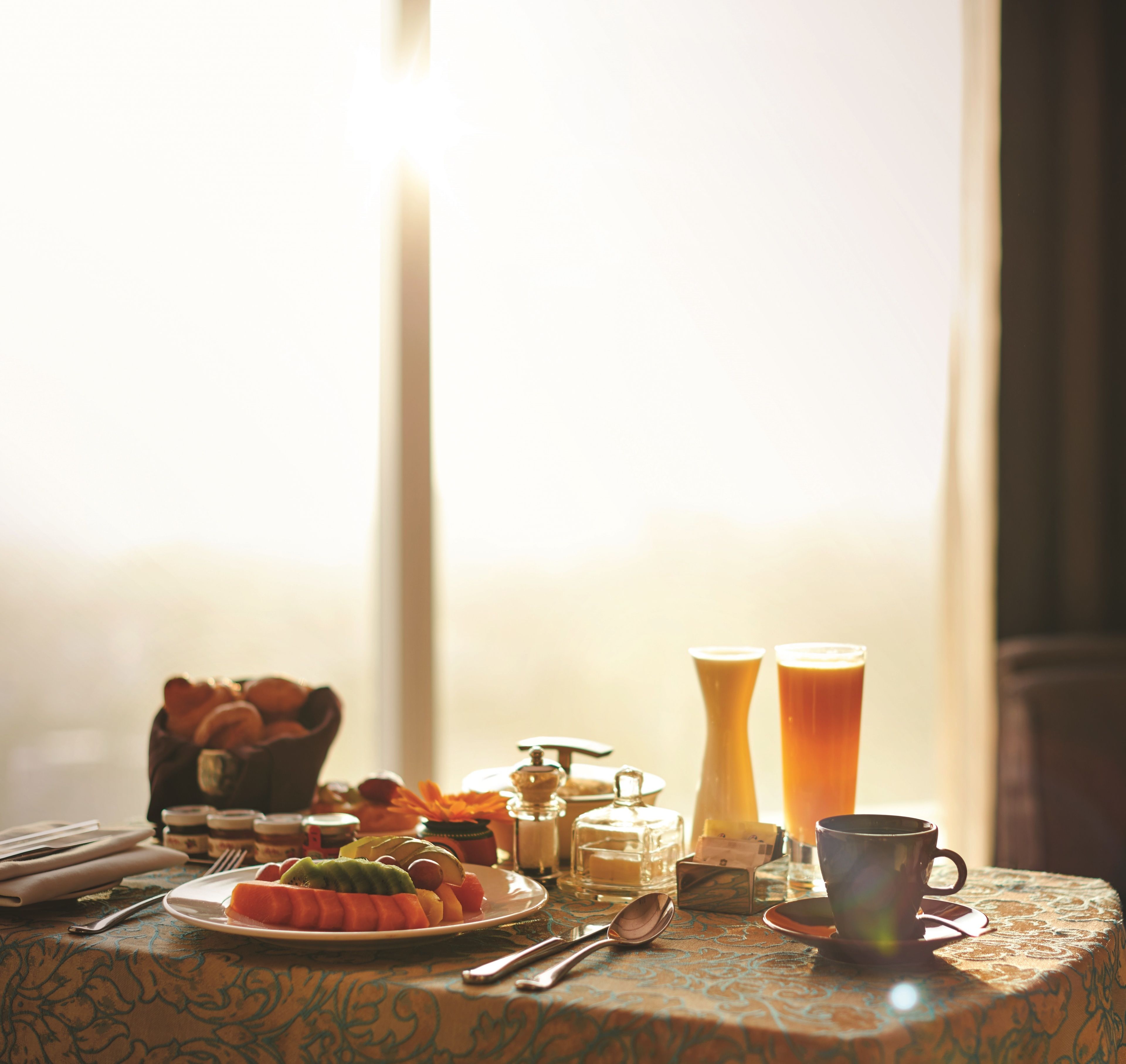 Ein Esstisch mit Früchten, einem Orangensaftglas und einer Tasse.