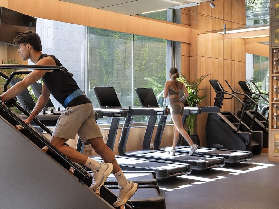 Ein modernes Fitnessstudio mit Laufbändern, auf einem davon ein Laptop und eine Person, die ein Laufband benutzt.