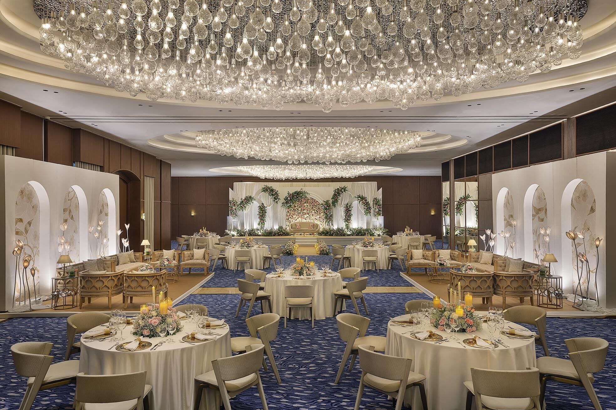 Ein Festsaal mit runden Tischen, Kronleuchtern und Blumendekorationen.