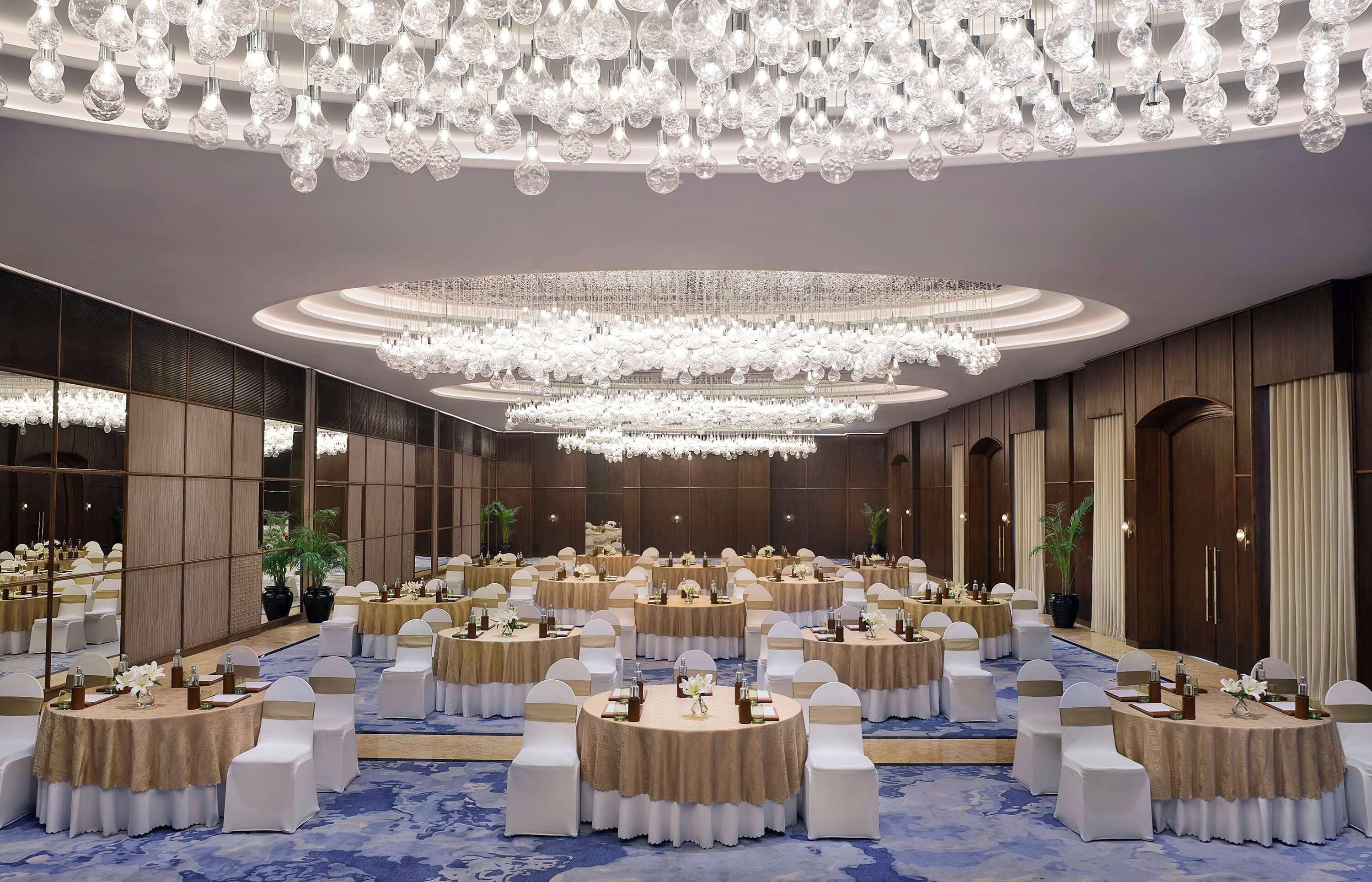 Une vaste salle de banquet avec des tables rondes, des chaises blanches et des lustres.