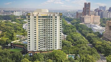A high-rise hotel with multiple floors, surrounded by lush greenery and a view of the cityscape in the background.