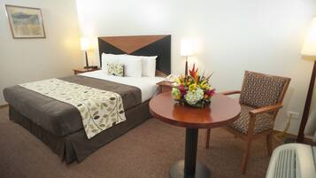 Une chambre d’hôtel avec un lit, une table ronde agrémentée d’un arrangement floral, une chaise et des lampes de chevet.