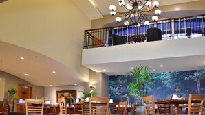 A spacious dining area with wooden tables and chairs, a chandelier, and a large mural of a forest. - Sleep Inn Hotel Paseo Las Damas (San José)