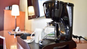 A coffee maker on a wooden table with a white mug and a remote control.