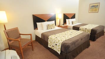 Habitación de hotel con dos camas, una silla, una mesita de noche y una lámpara.