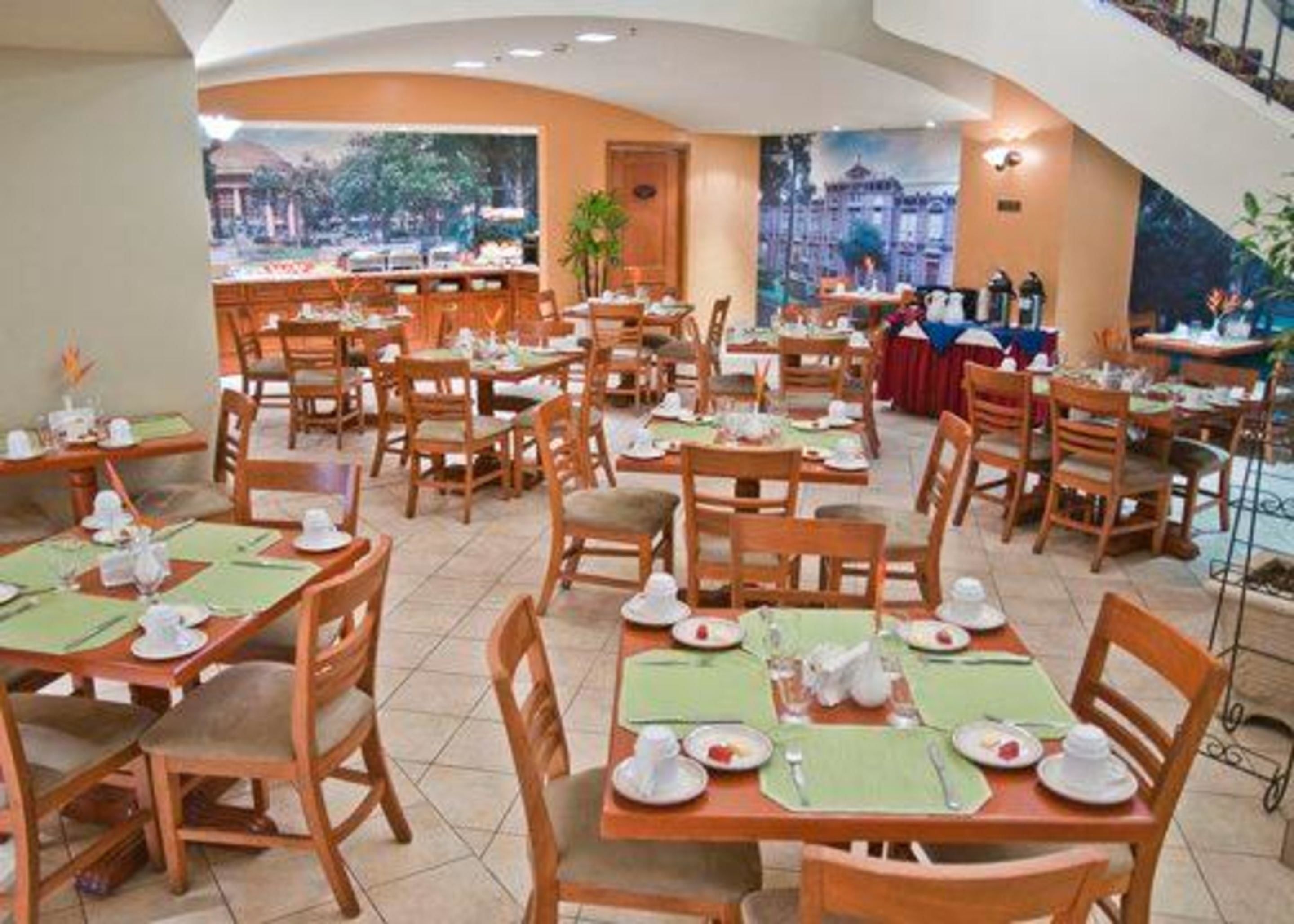 Um restaurante com várias mesas e cadeiras, disposto num espaço amplo e interior com grandes janelas.