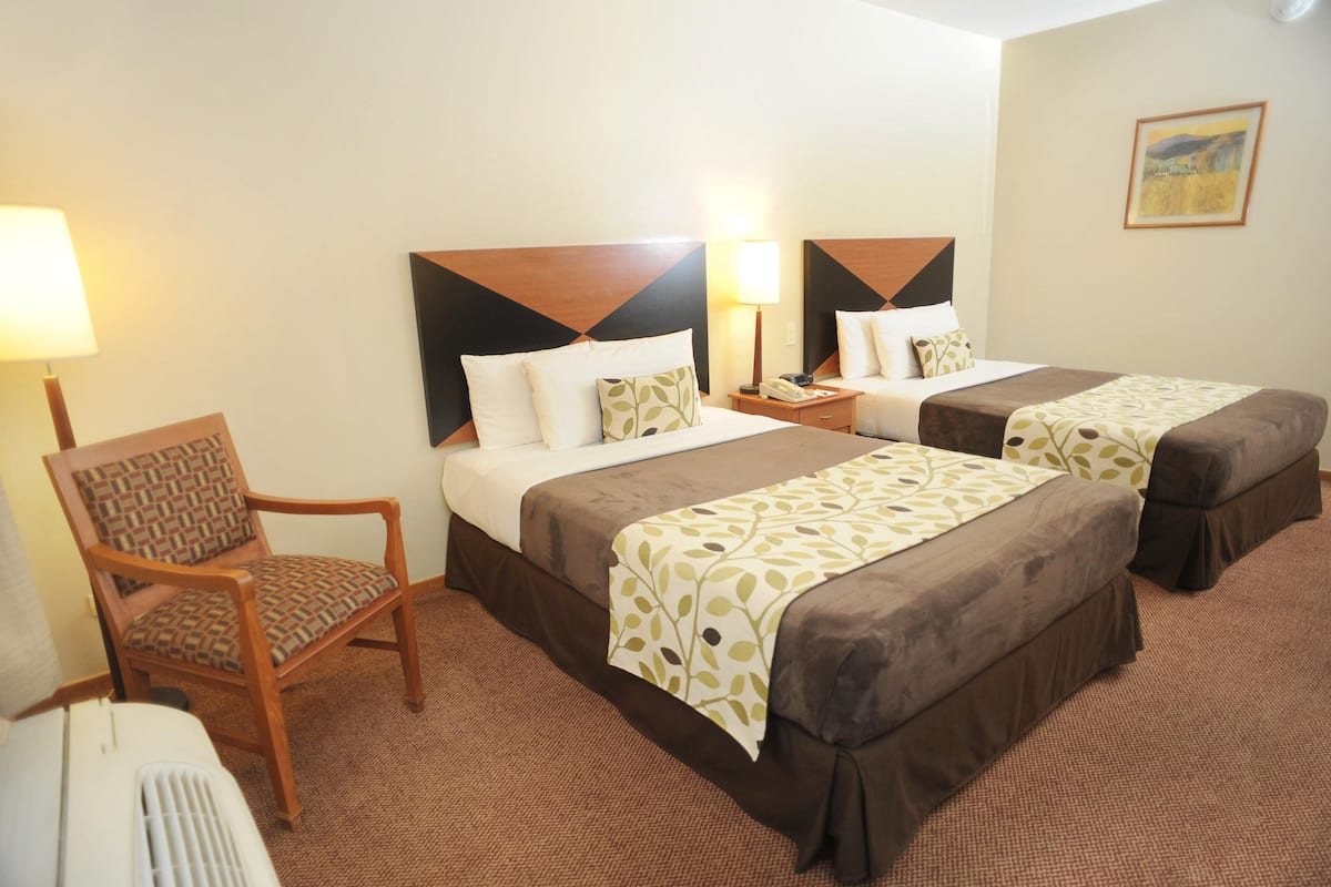 A hotel room with two beds, a chair, a nightstand, and a lamp.