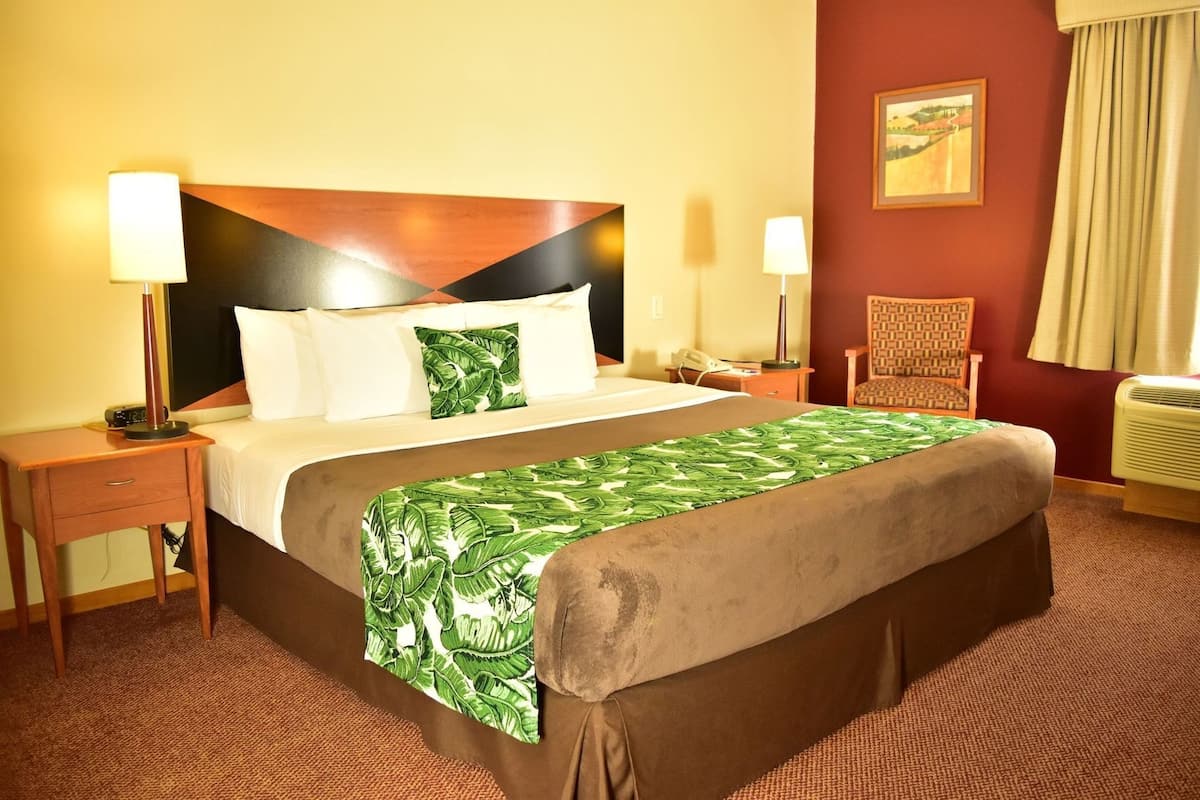 A hotel room with a bed, two bedside tables, a chair, a painting on the wall, and a window with curtains.