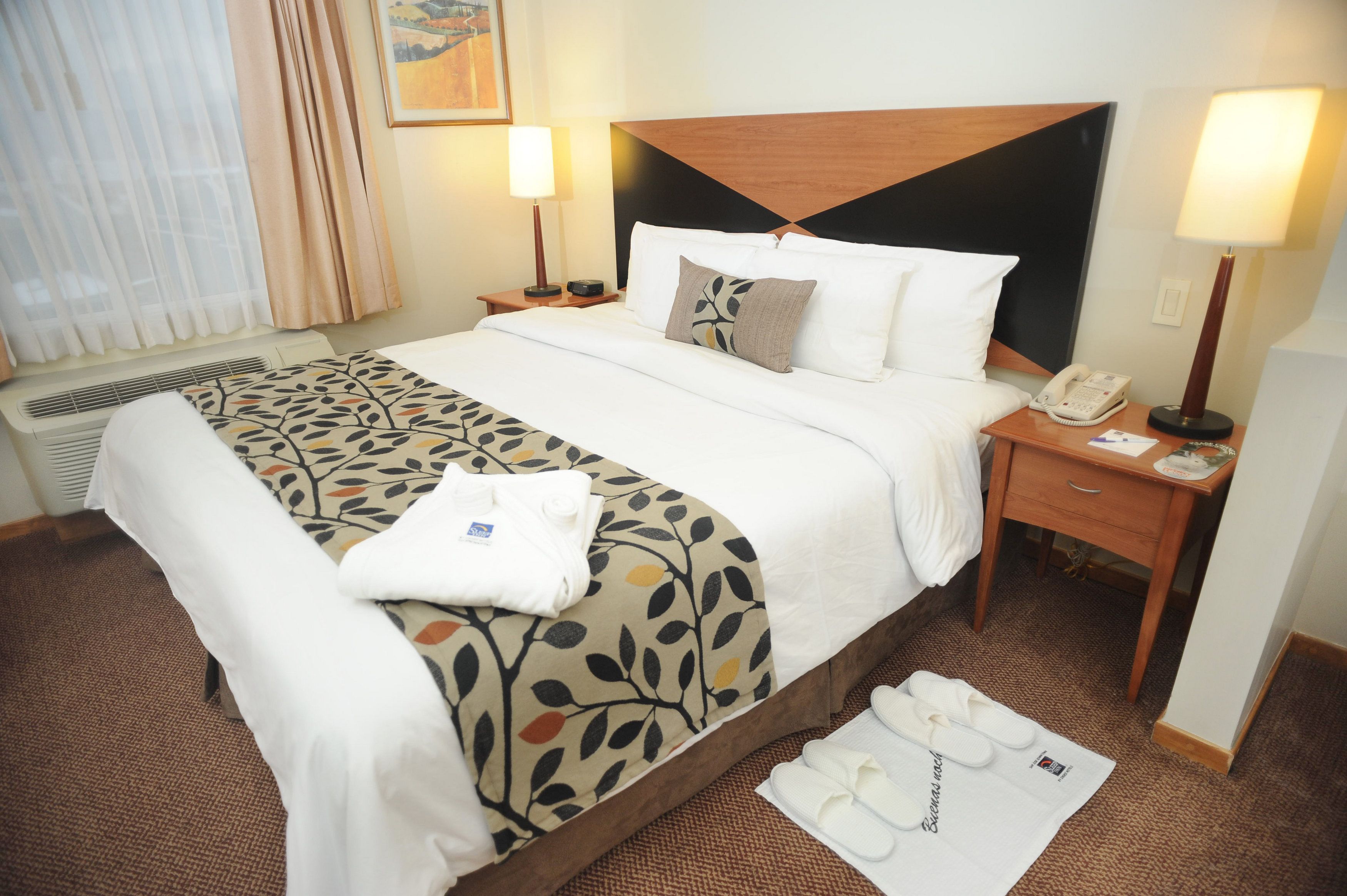 A hotel room with a bed, two bedside tables, a telephone, and a window with curtains.