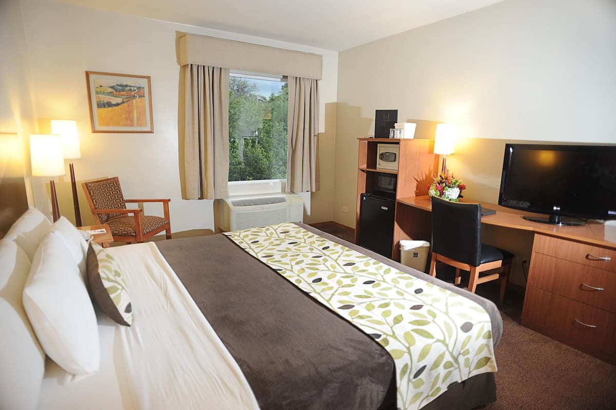A hotel room with a bed, desk, chair, television, and a window with curtains.
