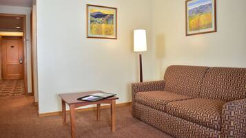 A hotel room with a patterned sofa, a small wooden table with a tablet, and two framed landscape paintings on the wall.