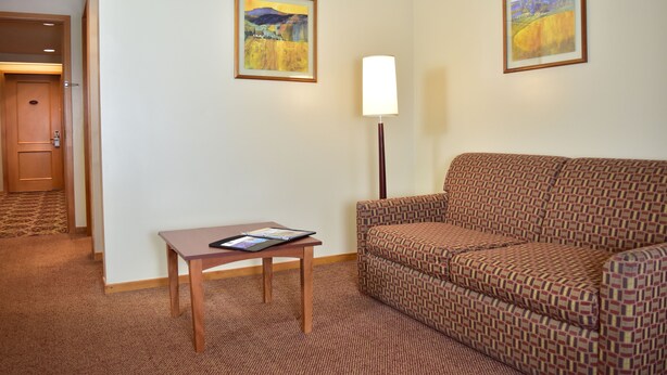 A hotel room with a patterned sofa, a small wooden table with a tablet, and two framed landscape paintings on the wall. - Sleep Inn Hotel Paseo Las Damas (San José)