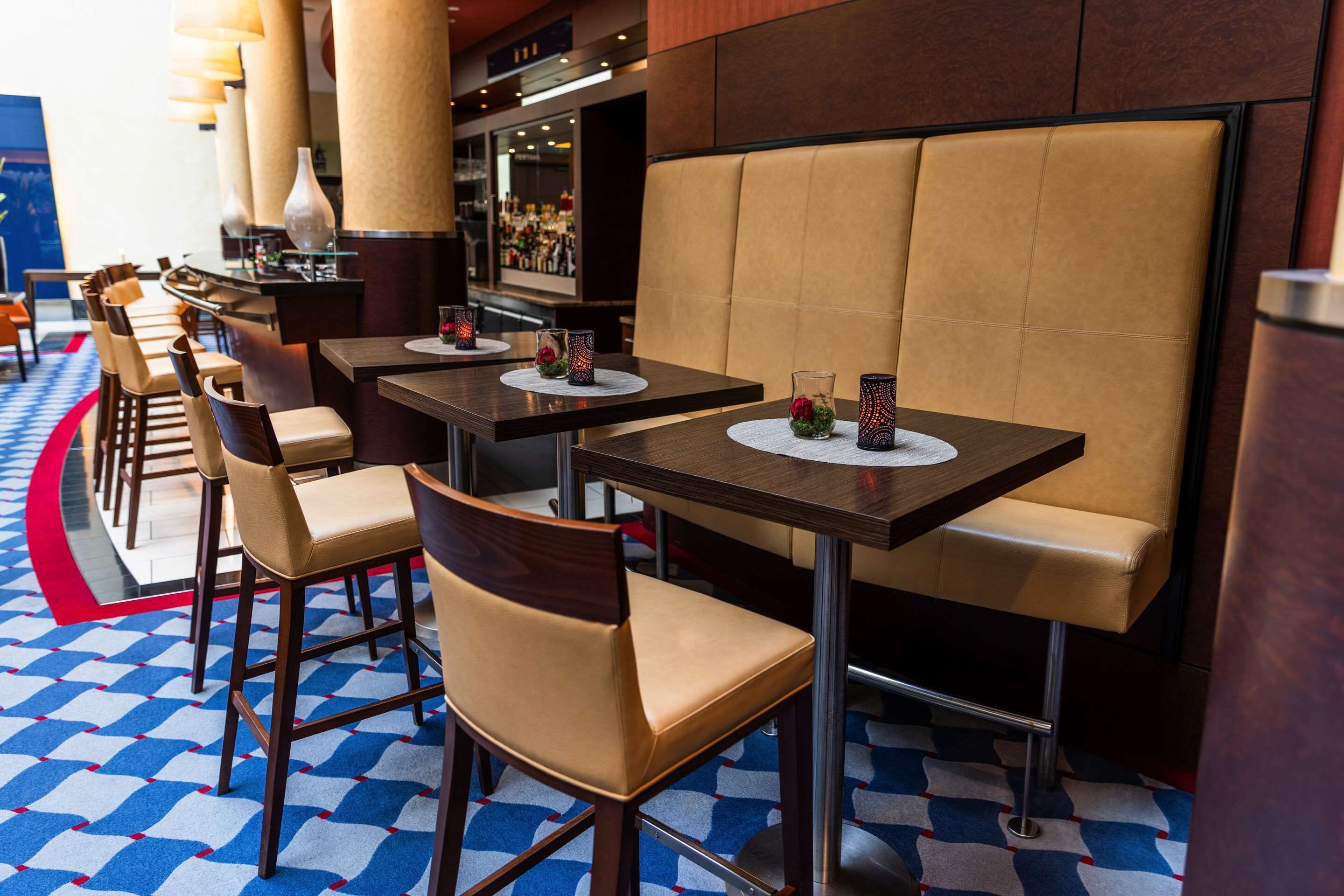 Een restaurant met zitjes, hoge tafels, een patroon vloer en een bar op de achtergrond.