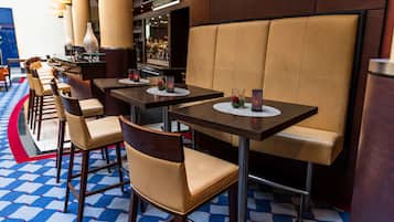 Een restaurant met zitjes, hoge tafels, een patroon vloer en een bar op de achtergrond.
