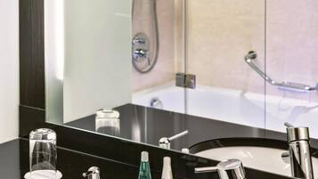 A modern bathroom with a black countertop, a round sink, two faucets, and a large mirror.