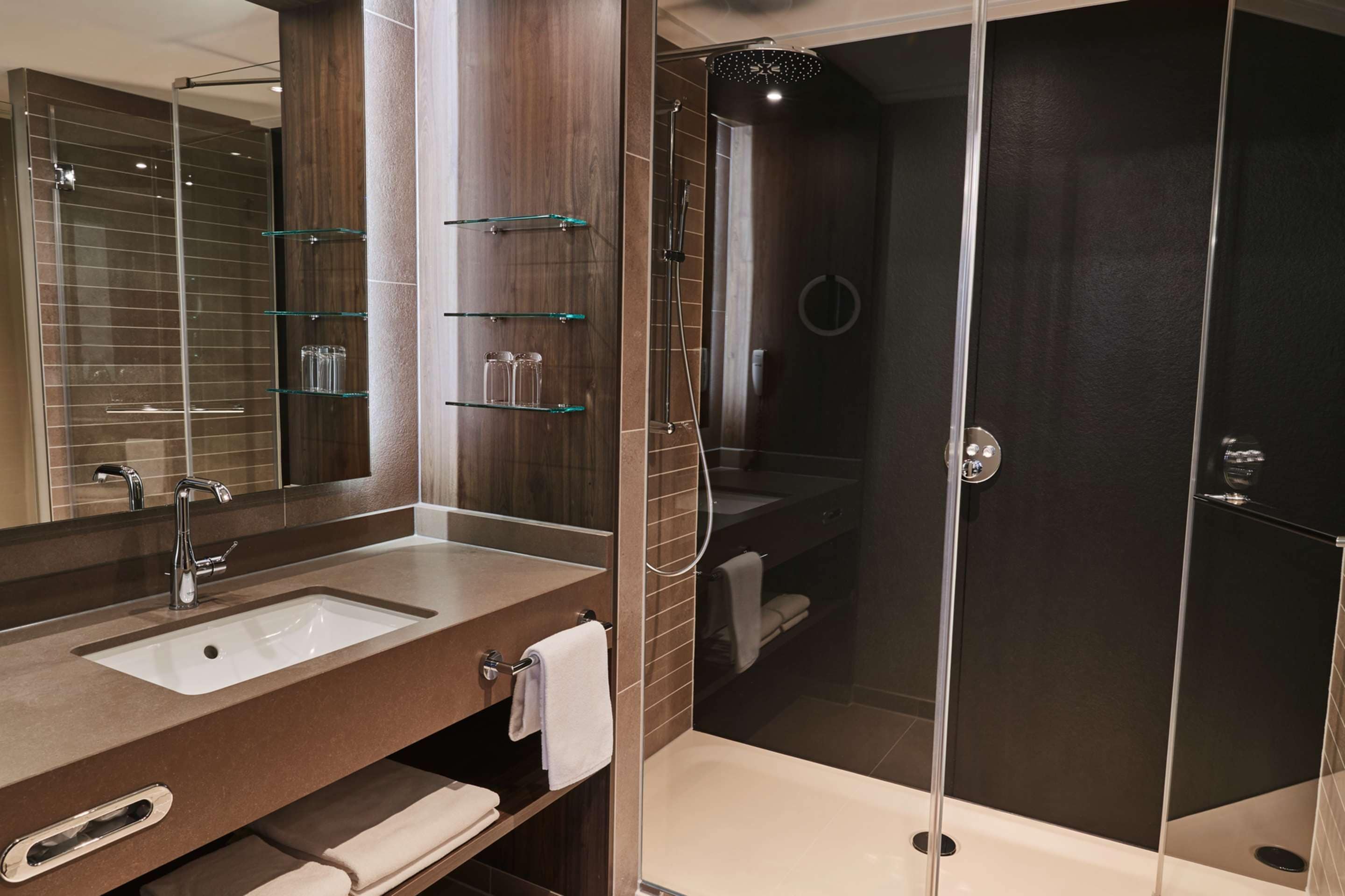 A modern bathroom with a large mirror, a sink, and a glass-enclosed shower.