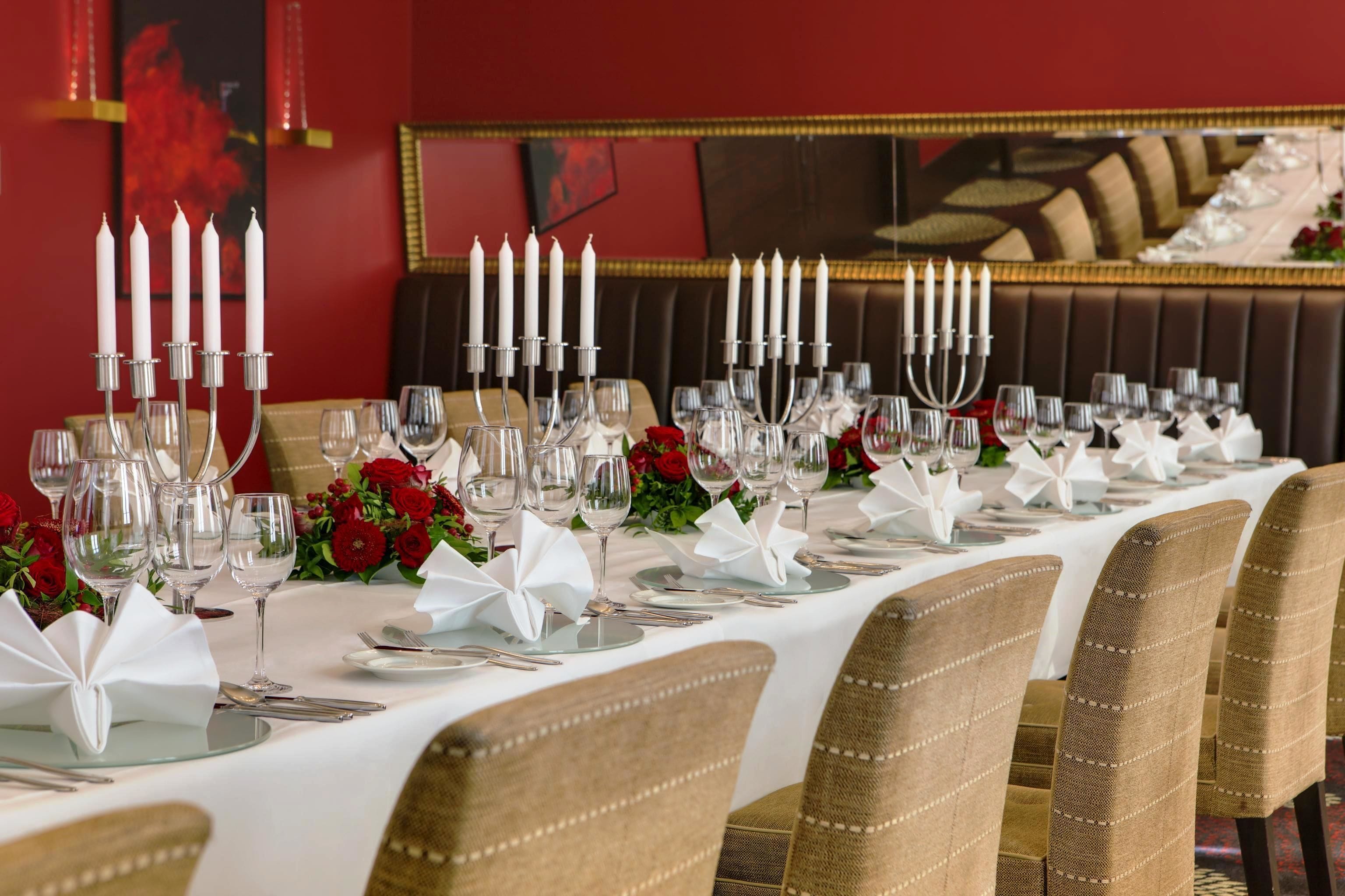 A long dining table set with white tablecloths, candles, and red flowers.