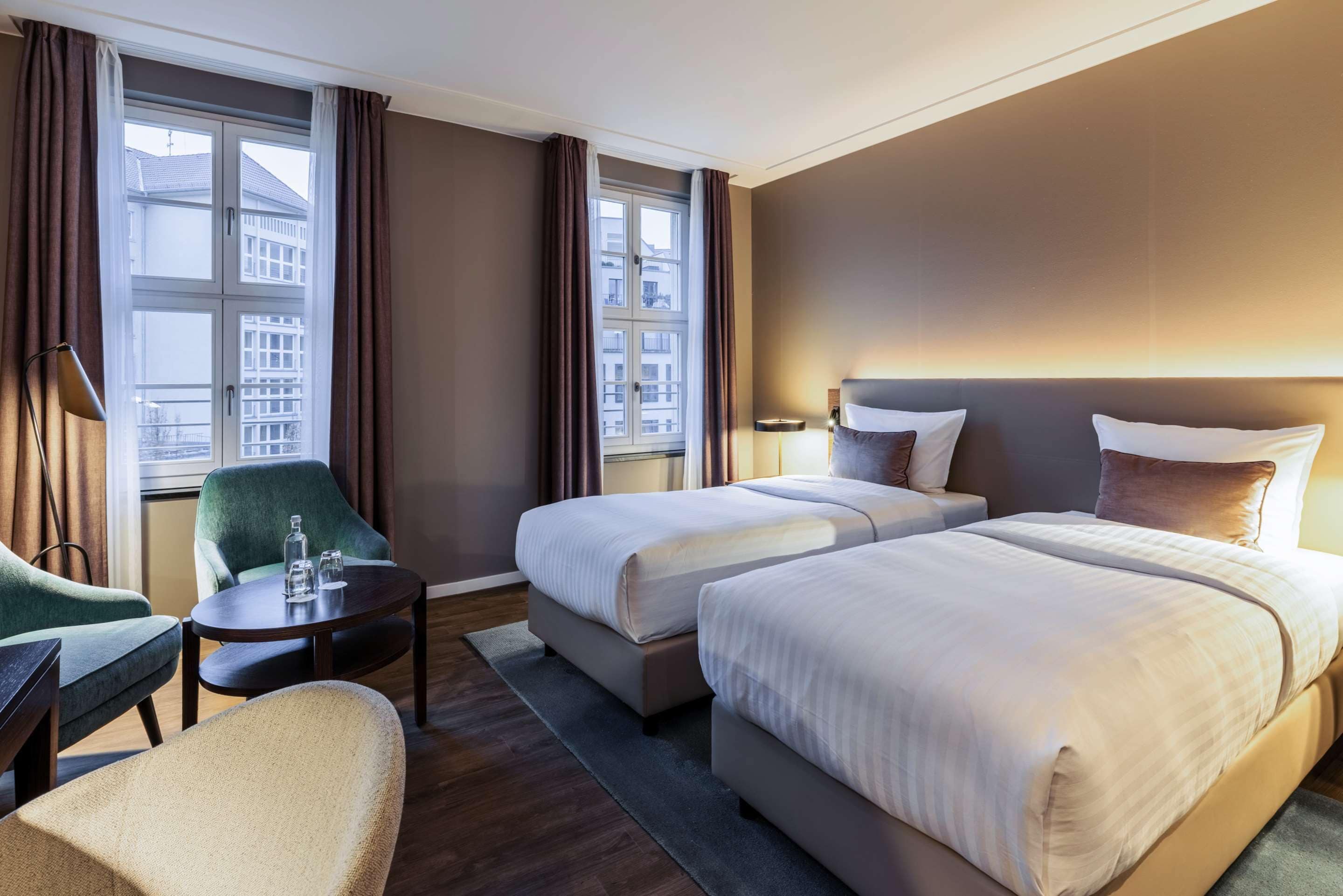 Hotelkamer met twee bedden, een bureau, een stoel en uitzicht op gebouwen.