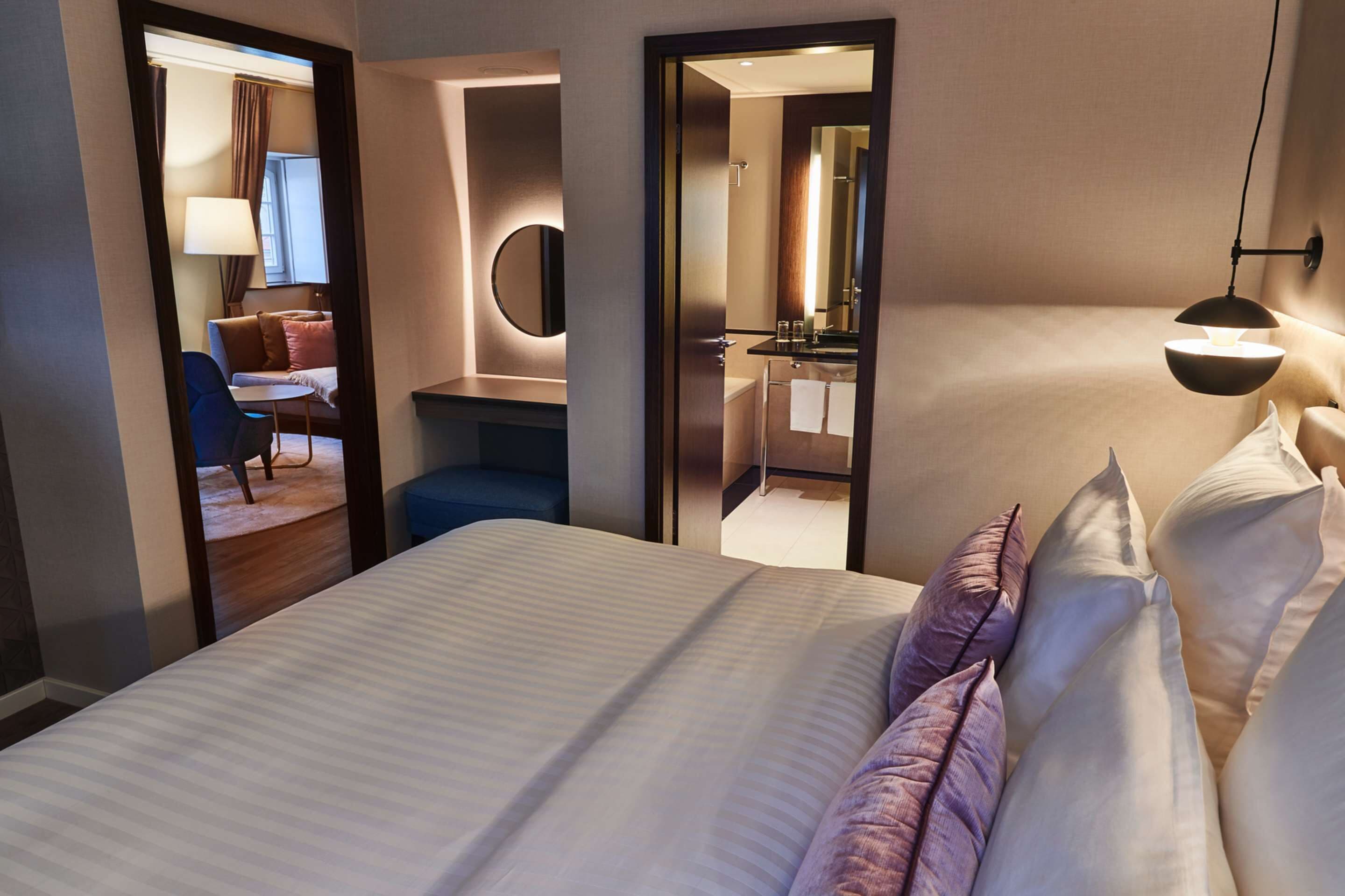 Hotelkamer met een groot bed, een bureau met stoel, een spiegel en een badkamer door een geopende deur zichtbaar.