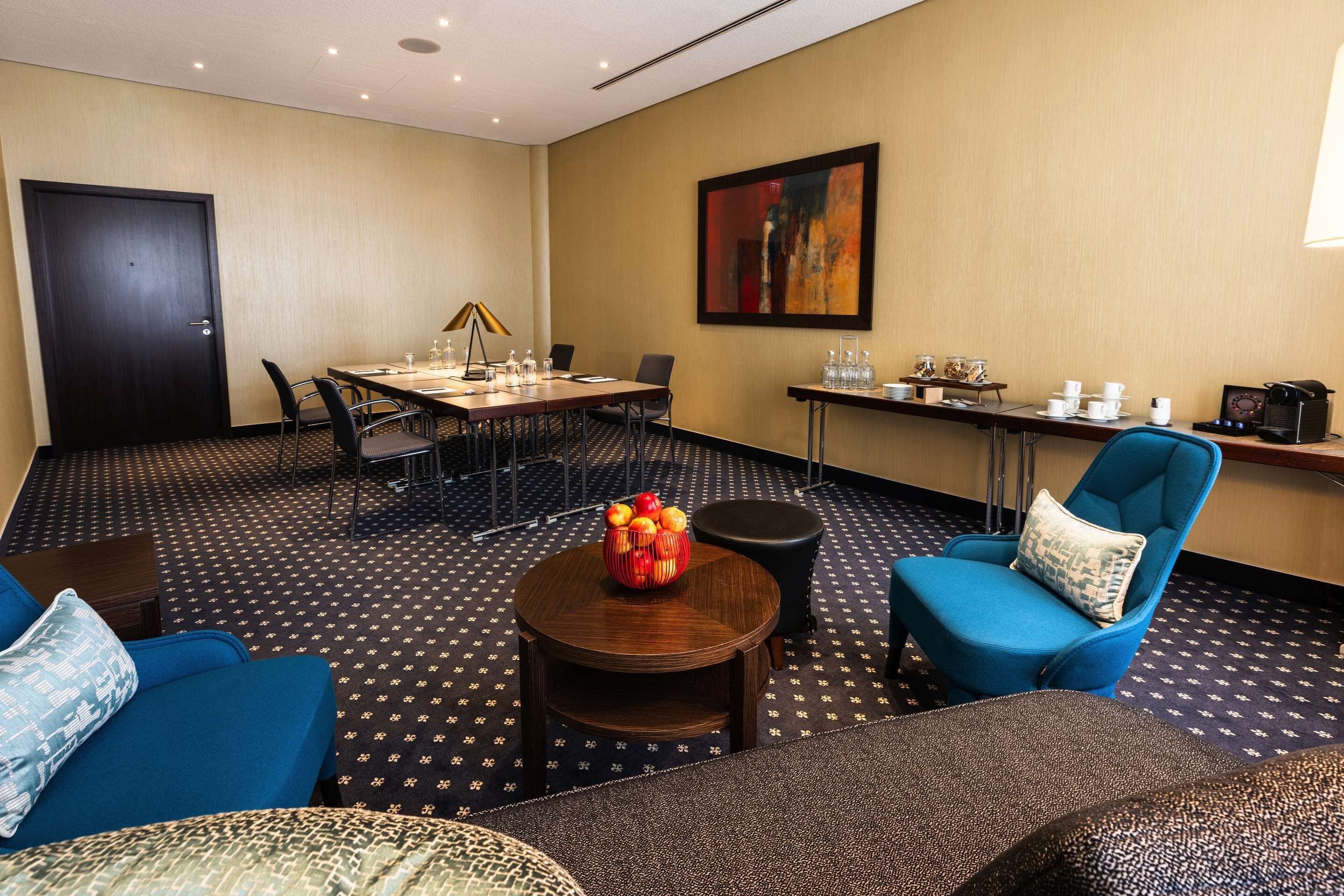 A conference room with a table, chairs, a coffee station, and a blue armchair.