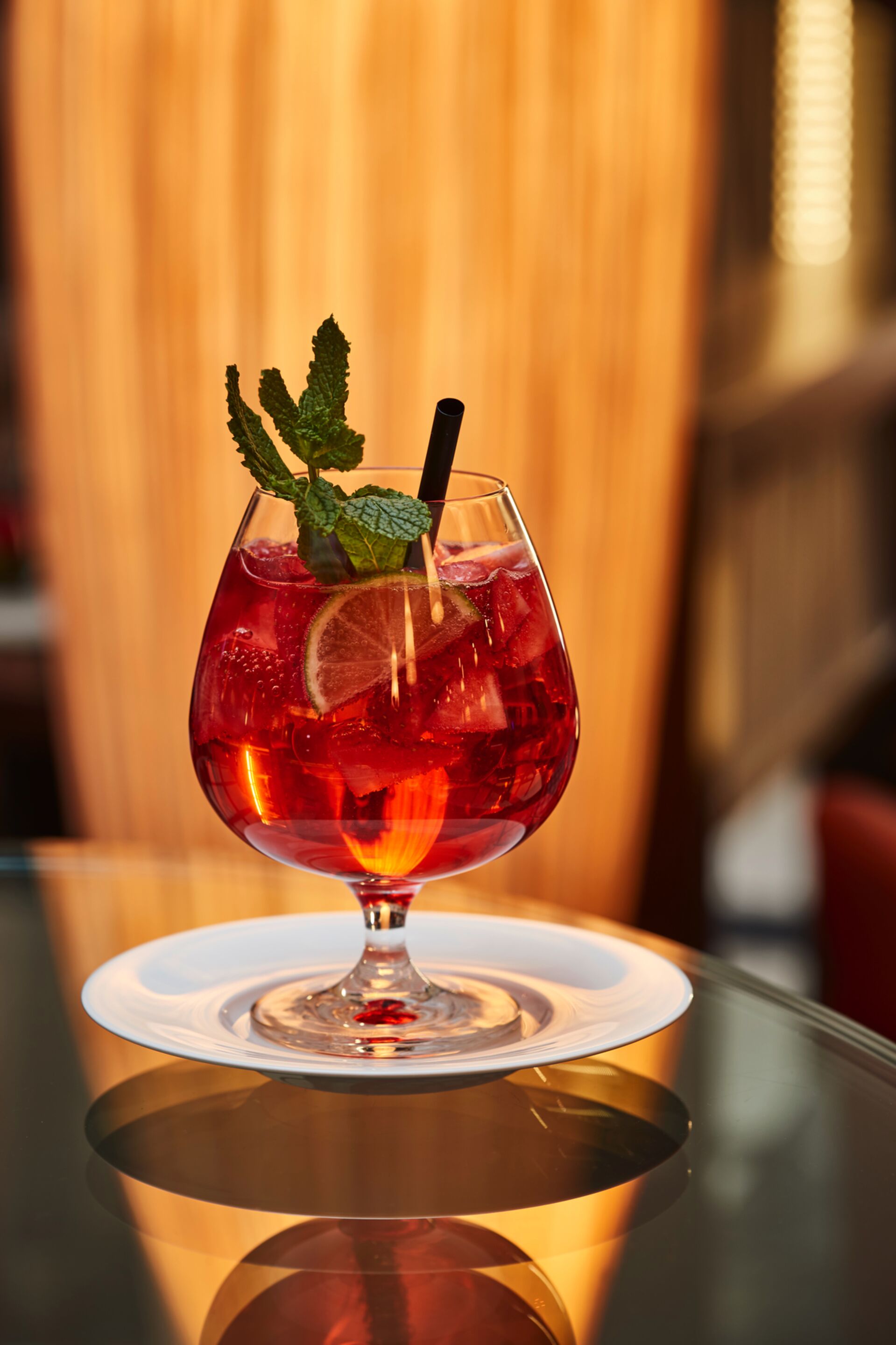 A cocktail glass with a red drink, garnished with mint and citrus, on a white coaster.