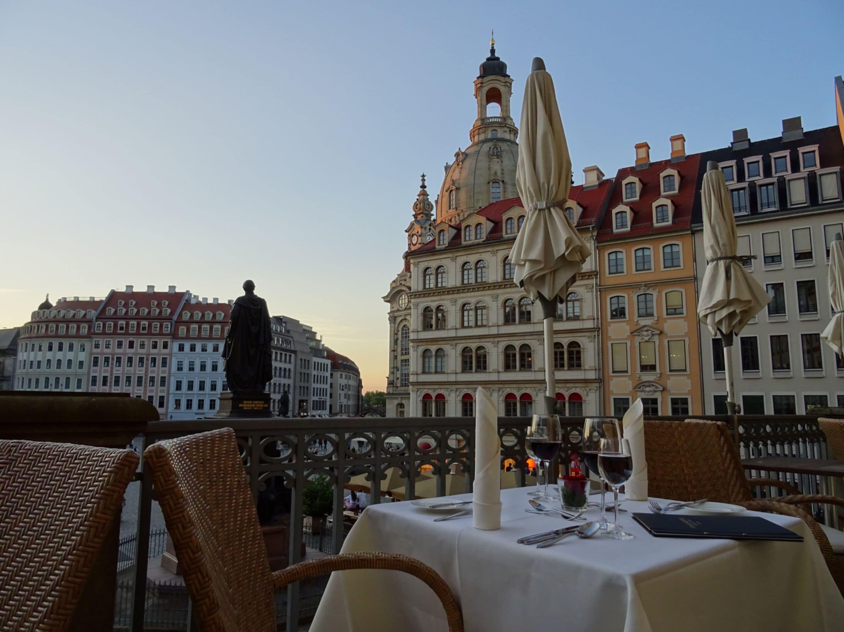A table set for dining with a view of historic buildings and a statue in the background.