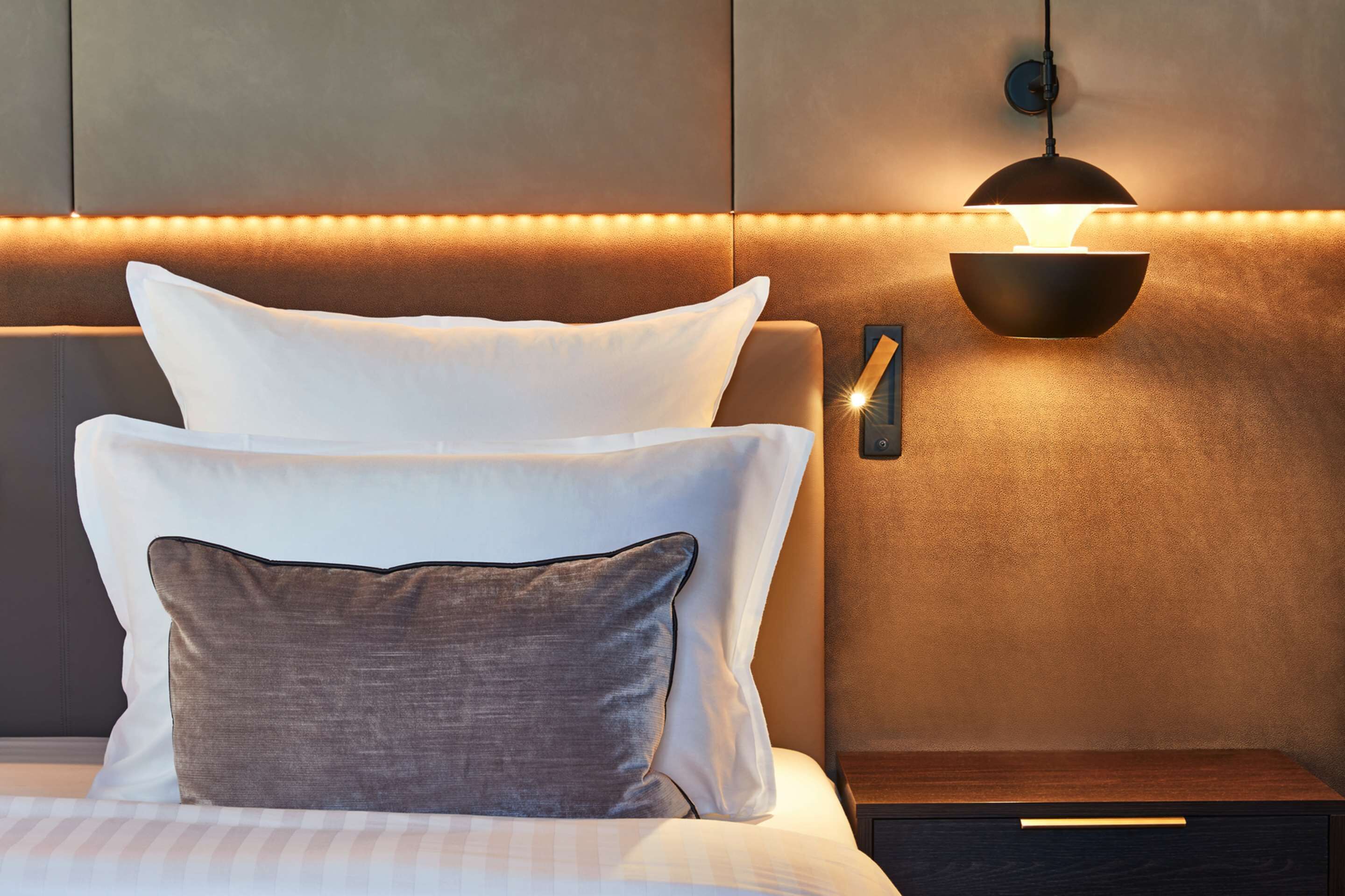 Habitación de hotel con una cama, una mesita de noche y una lámpara fijada a la pared.