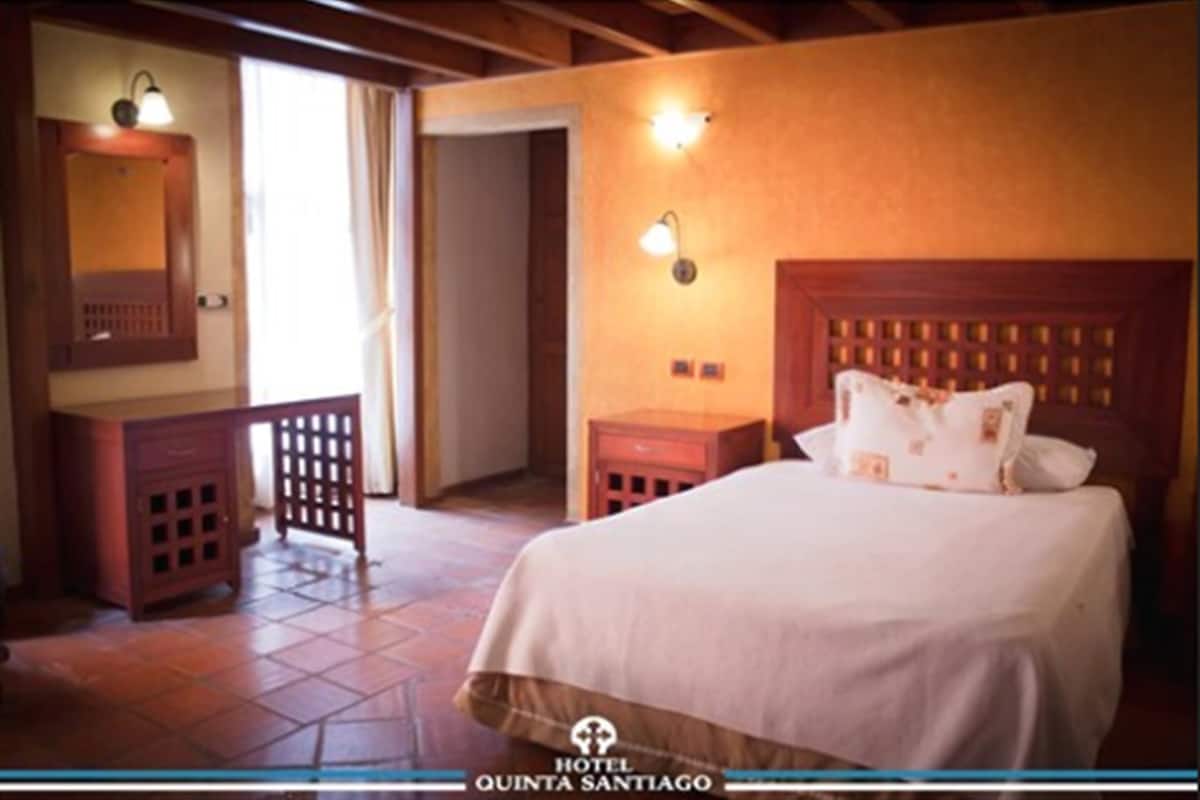 A hotel room with a bed, a nightstand, a dresser, a mirror, and two wall sconces.