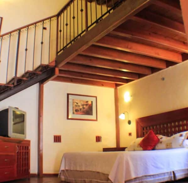 A bedroom with a wooden staircase, a bed with a white comforter, a red pillow, and a framed picture on the wall.