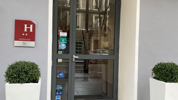 A hotel entrance with a grey door, a number 251 sign, a red 'H' sign, and two white planters. - Timhotel Boulogne Rives de Seine (Boulogne-Billancourt)