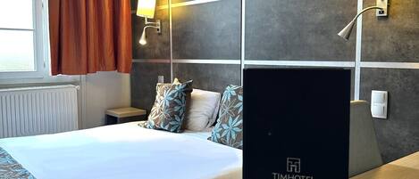 A hotel room with a large bed, two bedside lamps, a modern wall design, and a visible brand sign.