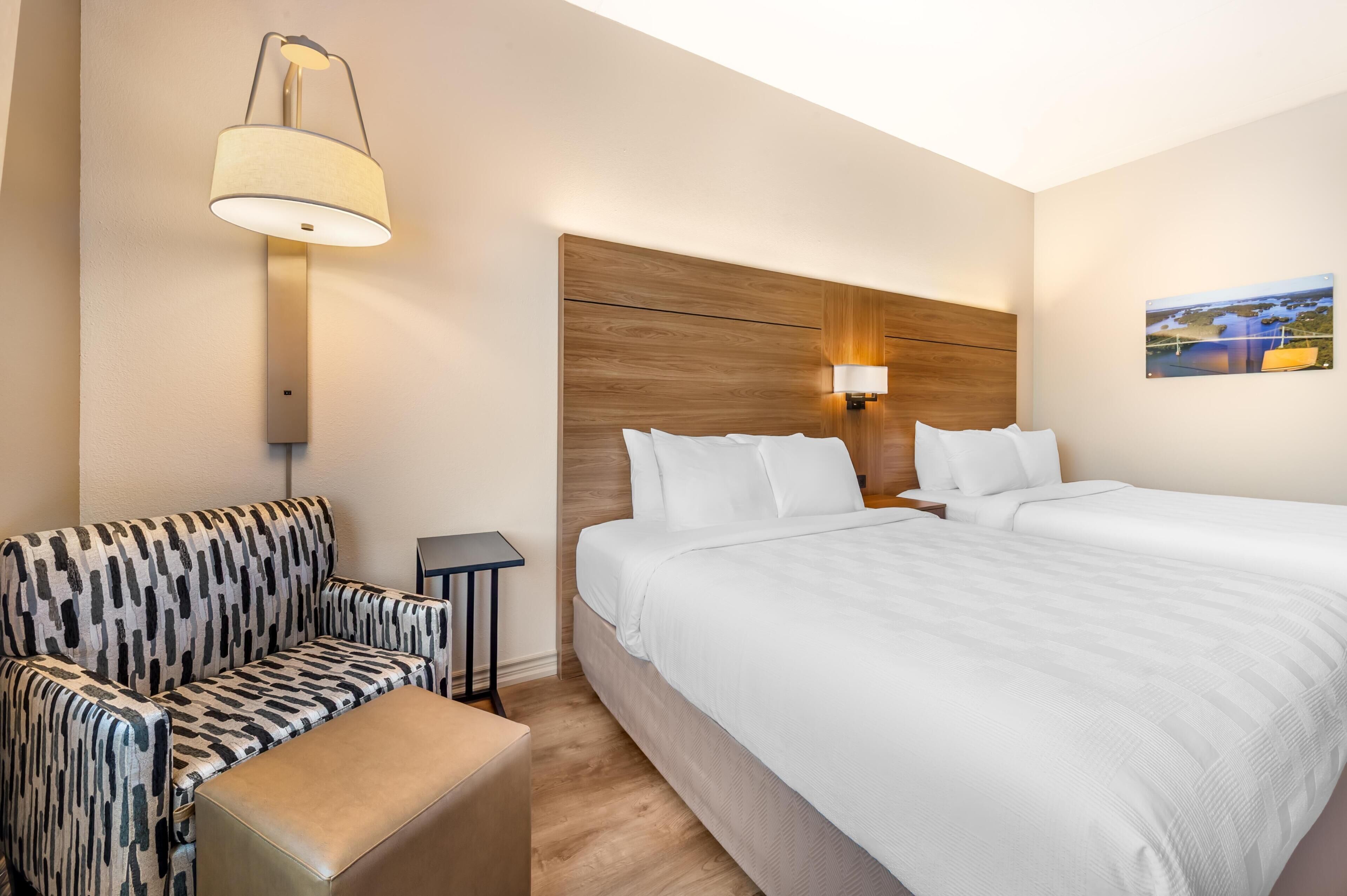 Habitación de hotel con cama, sofá, una mesita, lámpara e iluminación empotrada en la pared.