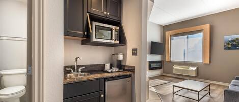 A compact kitchen with a microwave, sink, and dishwasher, a living area with a sofa and a TV, and a large window with a view.