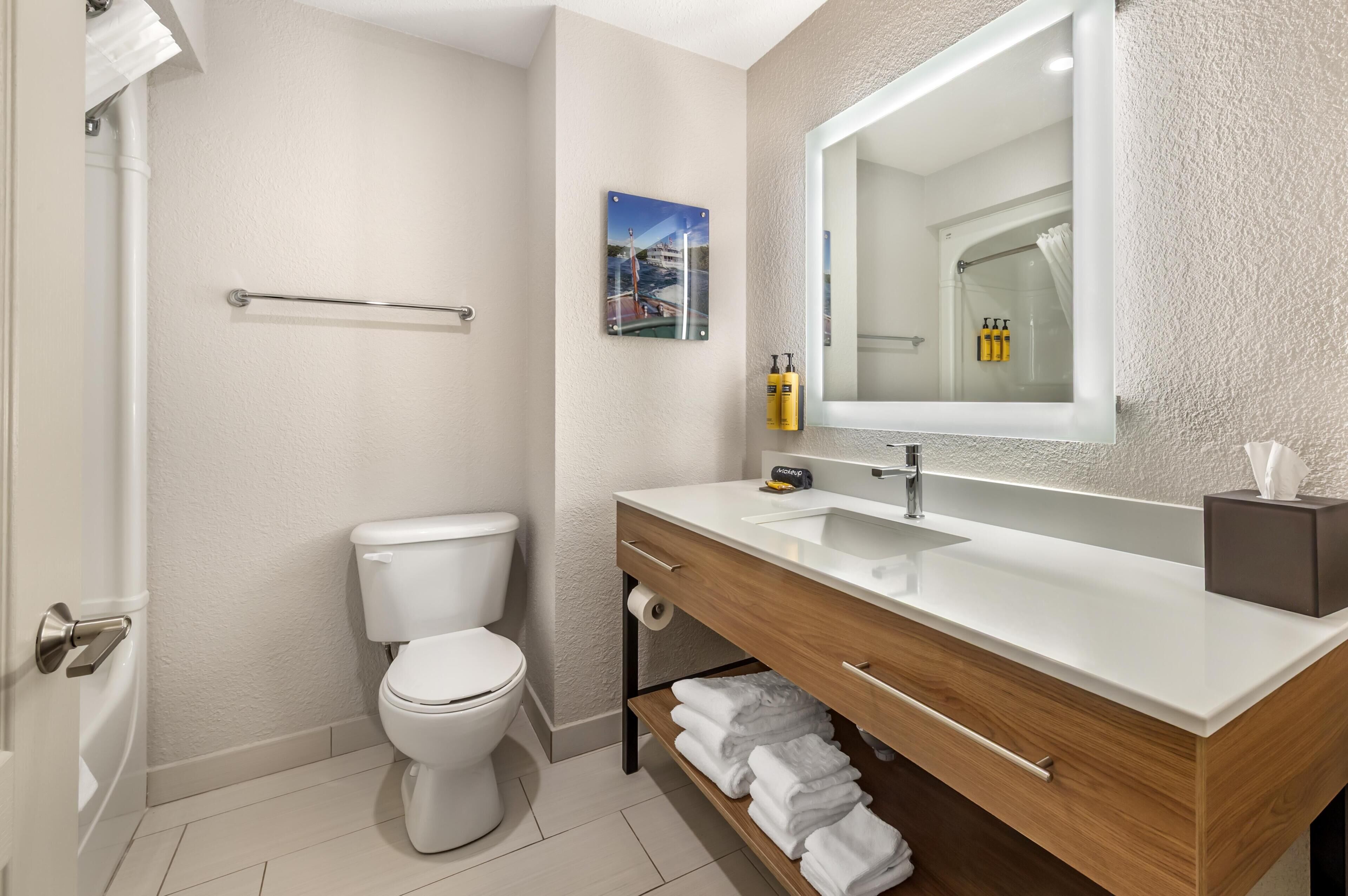 A bathroom with a toilet, a sink with a mirror, a towel rack, and a shelf with folded towels.