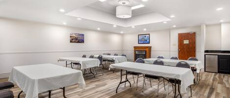 A conference room with tables, chairs, a fireplace, and a kitchenette.