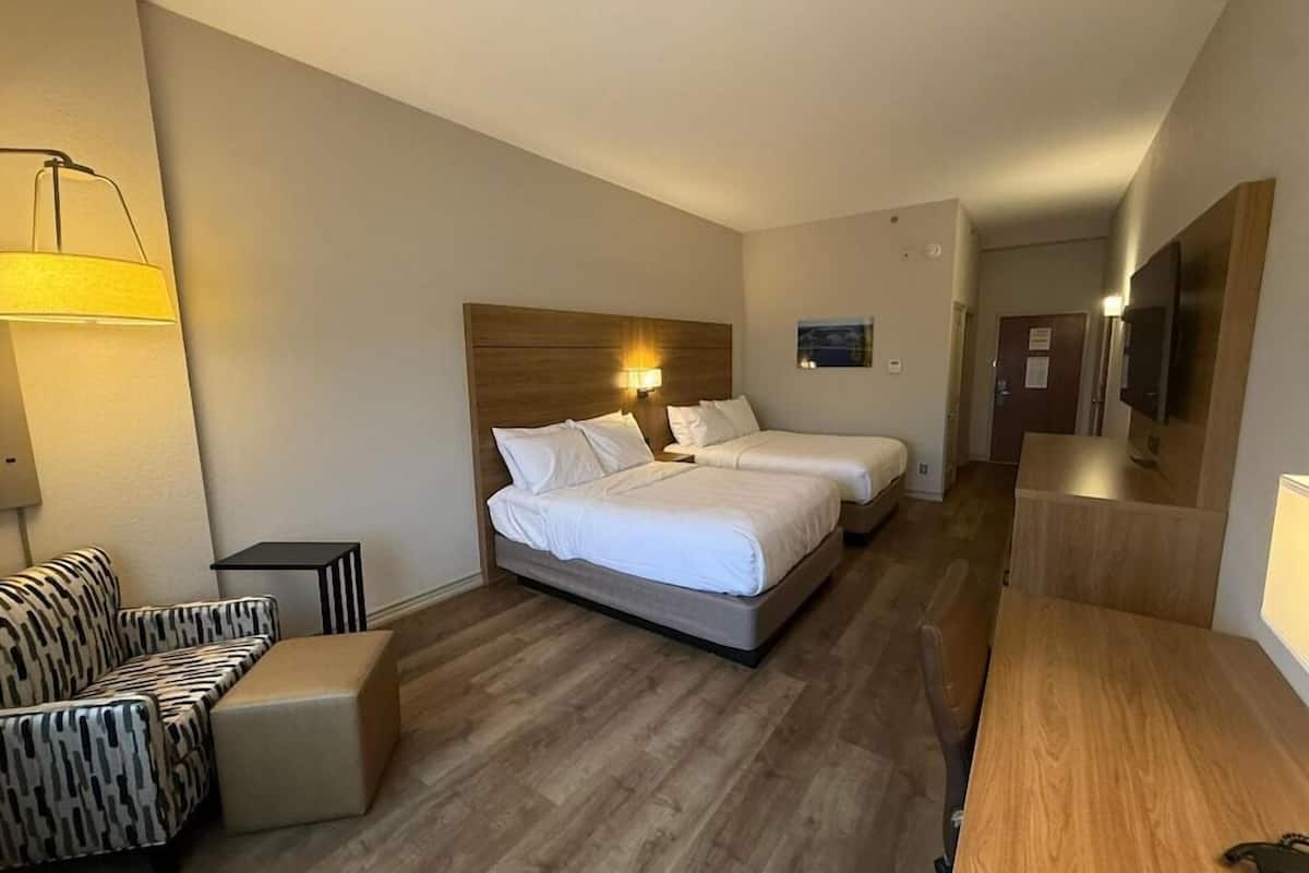 A hotel room with two beds, a sofa, a small table, and a TV.