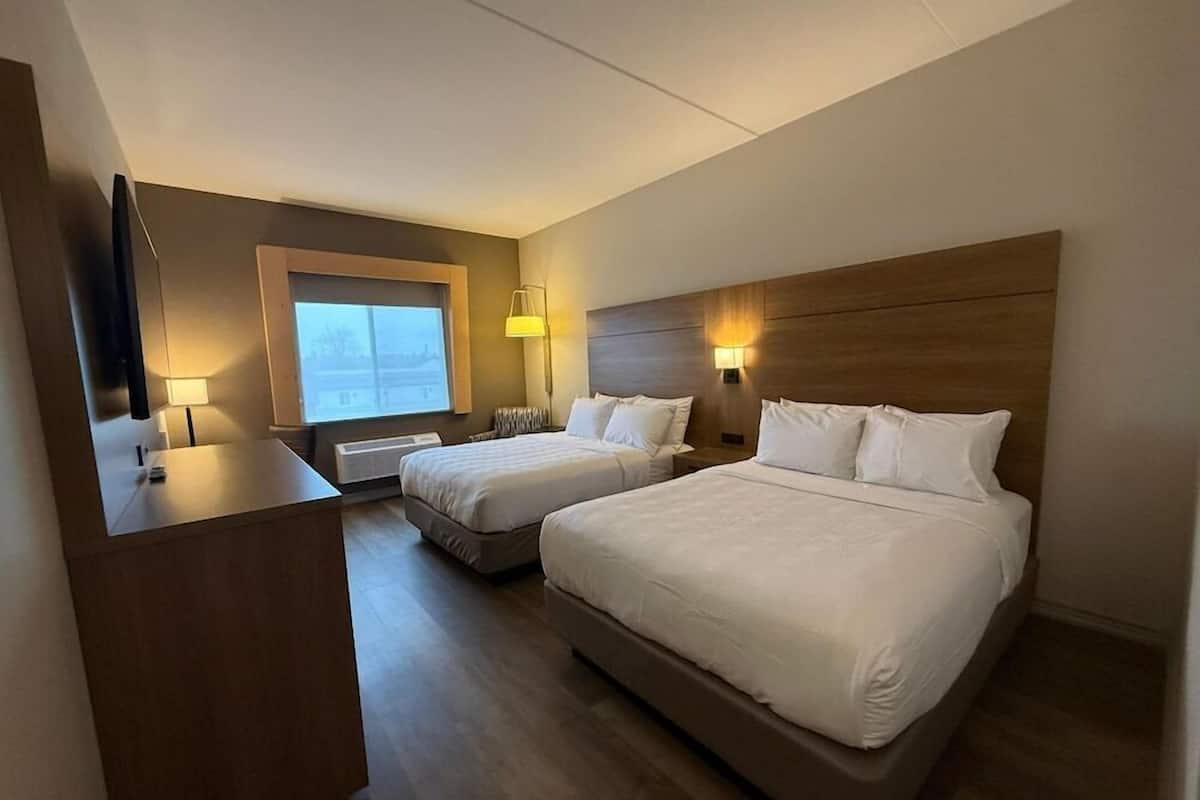 Une chambre d’hôtel avec deux lits, un bureau, une fenêtre et des lampes fixées au mur.