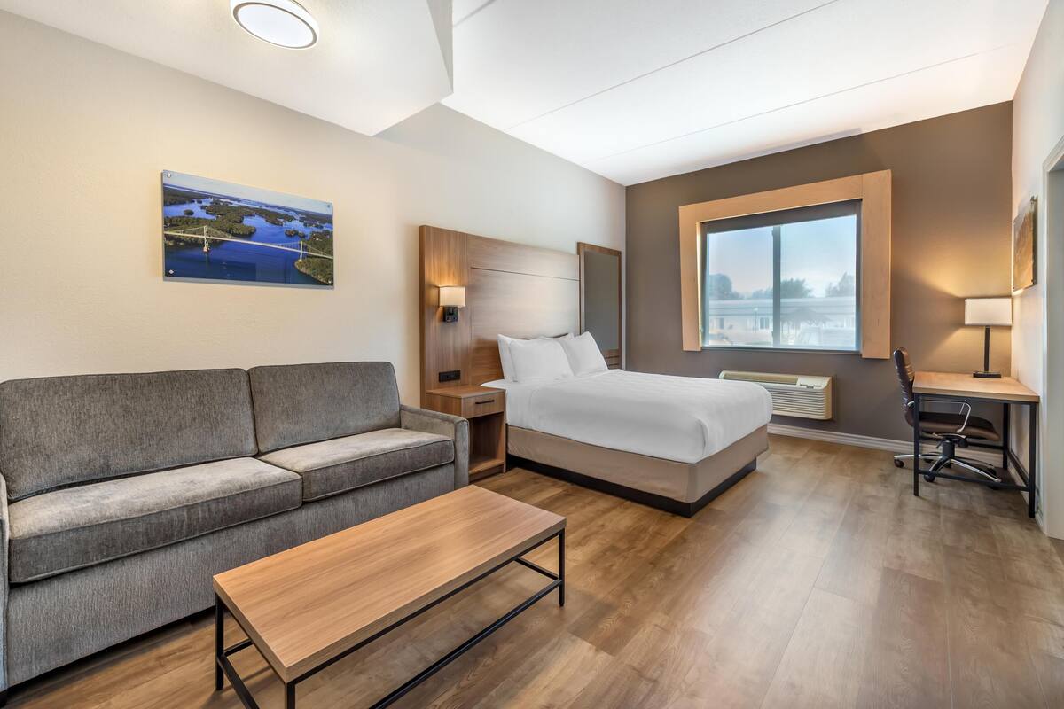 A hotel room with a bed, a sofa, a desk, and a window.