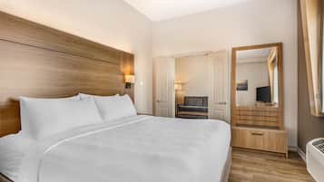 A hotel room with a large bed, a wooden headboard, a mirror, a seating area, and a door leading to another room.