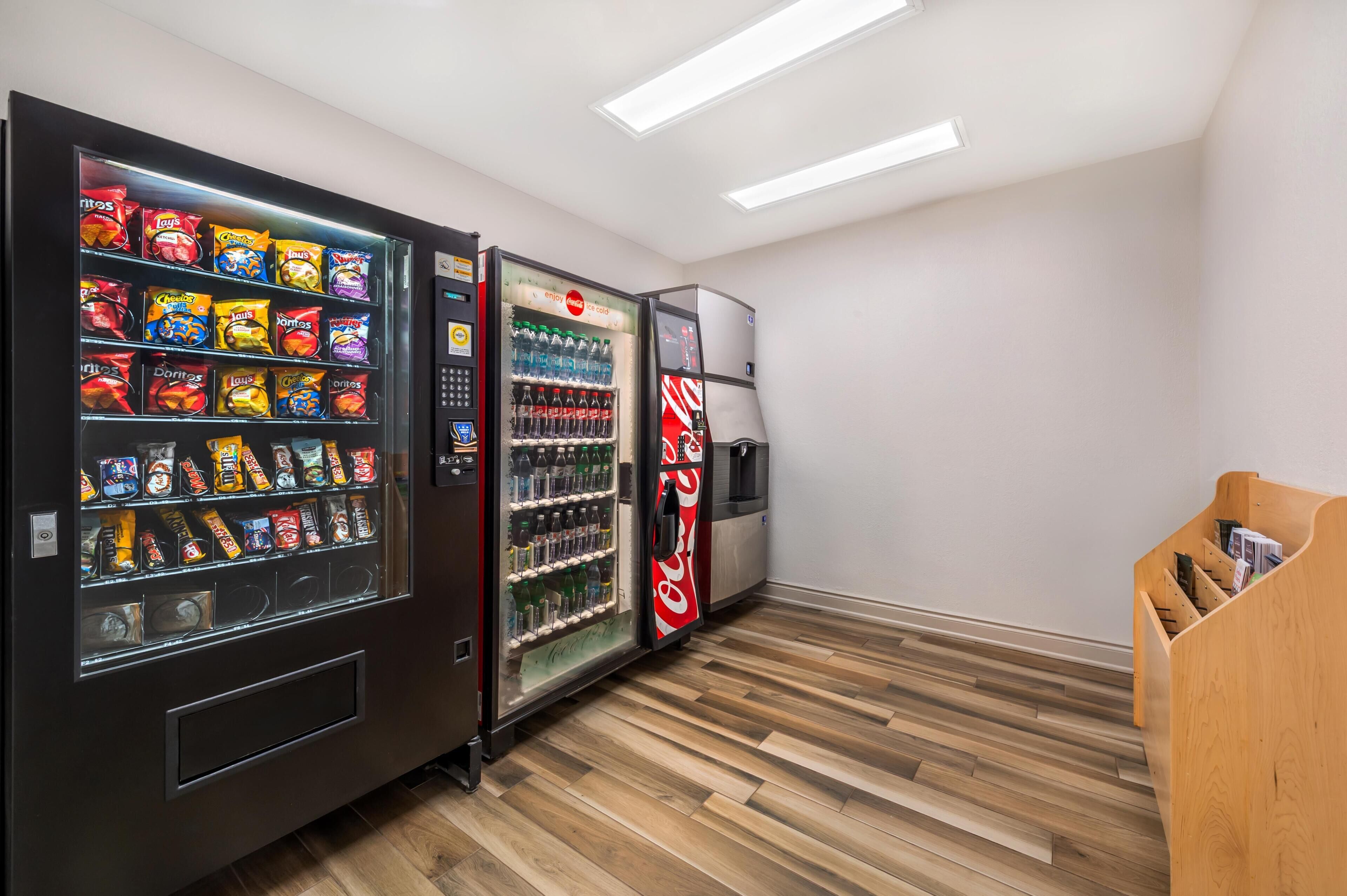 A vending machine area with snack and drink options, a Coca-Cola refrigerator, and a wooden bench.