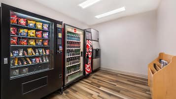 A vending machine area with snack and drink options, a Coca-Cola refrigerator, and a wooden bench.