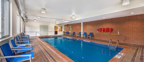 Una piscina interna con sedie blu, un muro in mattoni e un soffitto con illuminazione a incasso.