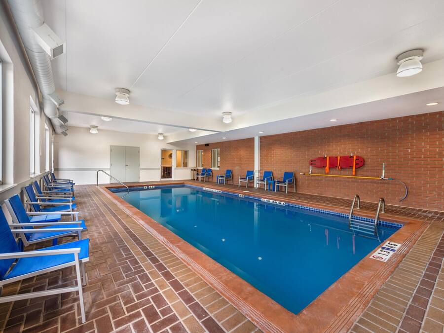 An indoor swimming pool with blue chairs, a brick wall, and a ceiling with recessed lighting.