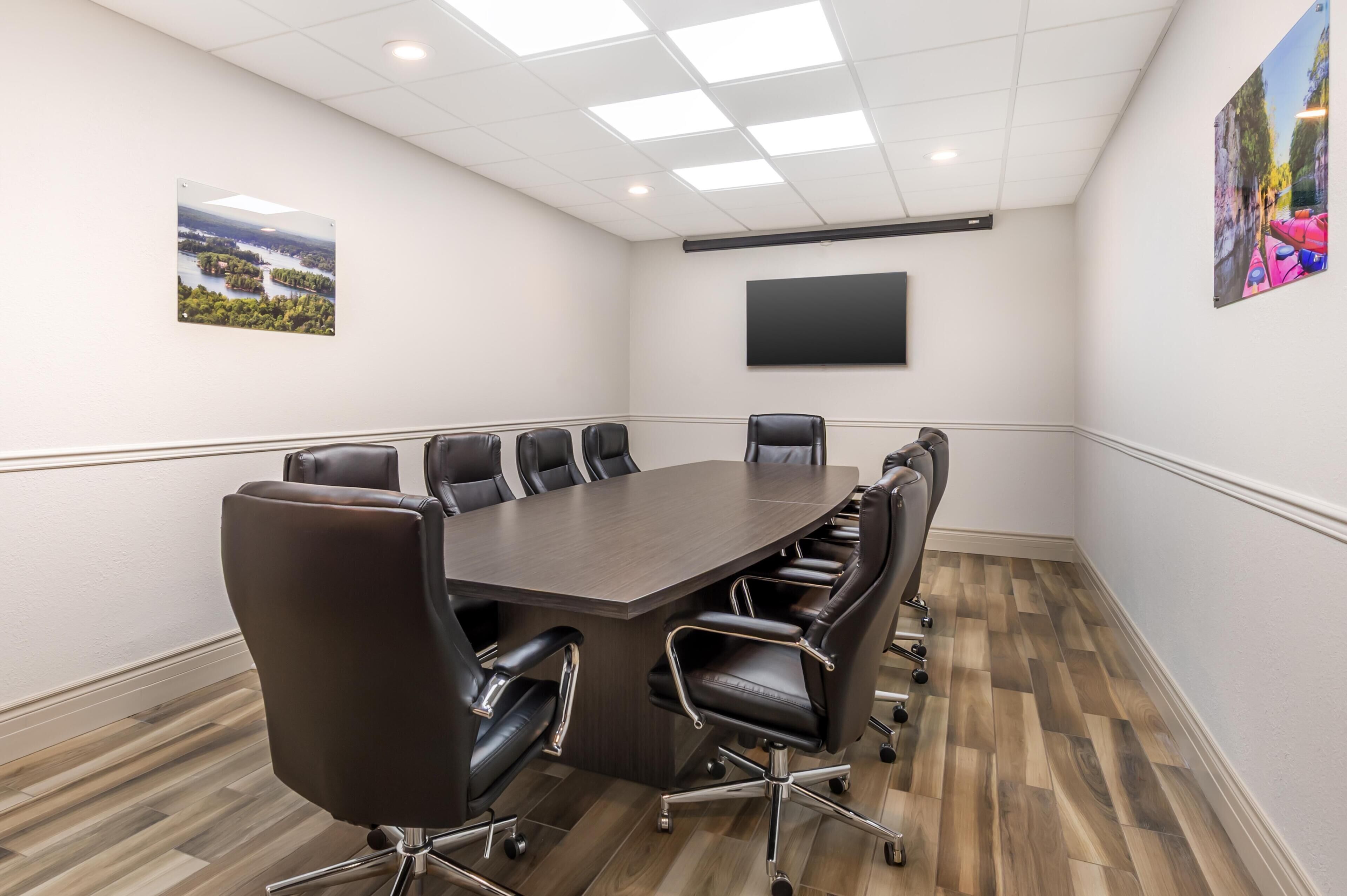 A conference room with a large table, multiple chairs, a flat-screen TV, and framed pictures on the walls.